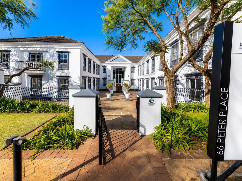 A well-maintained commercial office complex entrance featuring a paved walkway, landscaped gardens, and a prominent signage pillar at 66 Peter Place.