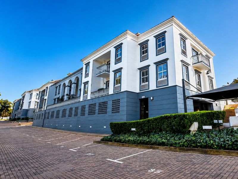A well-maintained multi-story commercial building featuring a paved parking area, structured facade with balconies, and neat landscaping.