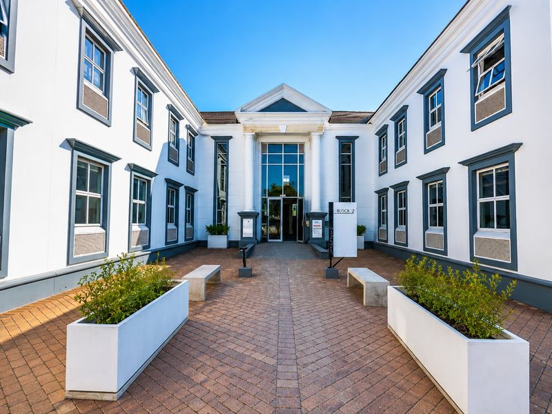 A well-maintained commercial office building entrance featuring a paved courtyard, classical architectural details, and a prominent glass facade.