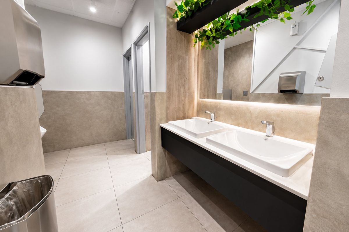 Modern commercial bathroom featuring a sleek double vanity with integrated sinks, backlit mirror, and contemporary tiled finishes.