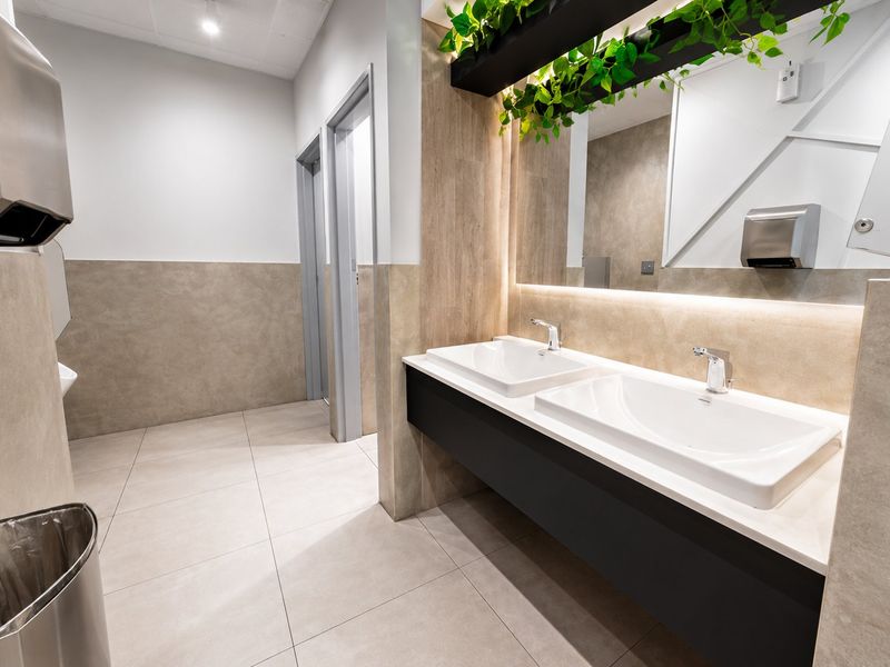 Modern commercial bathroom featuring a sleek double vanity with integrated sinks, backlit mirror, and contemporary tiled finishes.