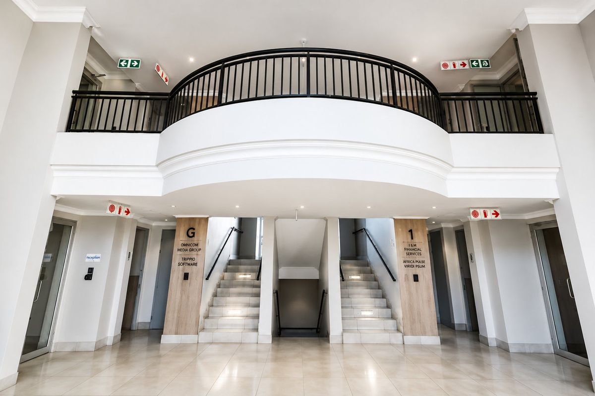 Modern commercial building entrance featuring a double-volume foyer, tiled flooring, and a central staircase with metal balustrades leading to upper levels.