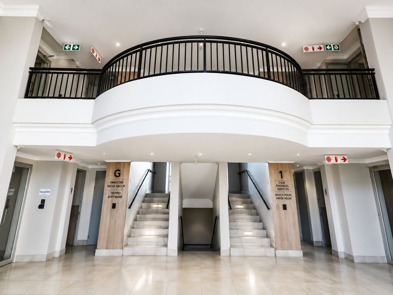 Modern commercial building entrance featuring a double-volume foyer, tiled flooring, and a central staircase with metal balustrades leading to upper levels.