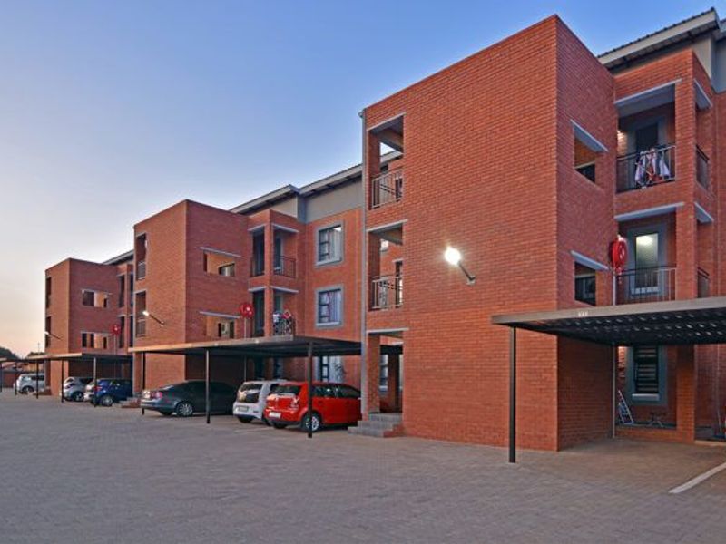 A multi-story apartment complex featuring face brick construction, covered parking bays, and private balconies for each unit.