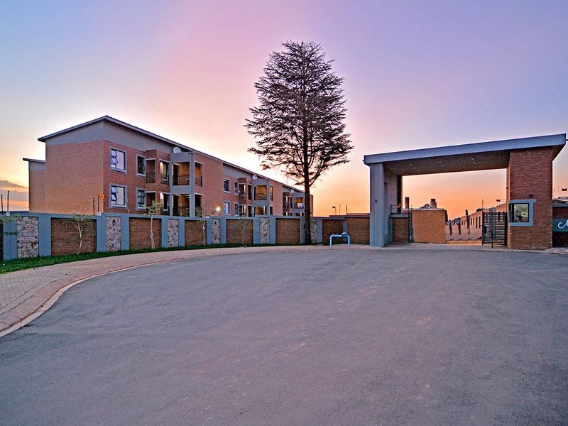 Front exterior view of the apartment complex featuring a secure gated entrance, brick facade, and paved driveway at sunset.