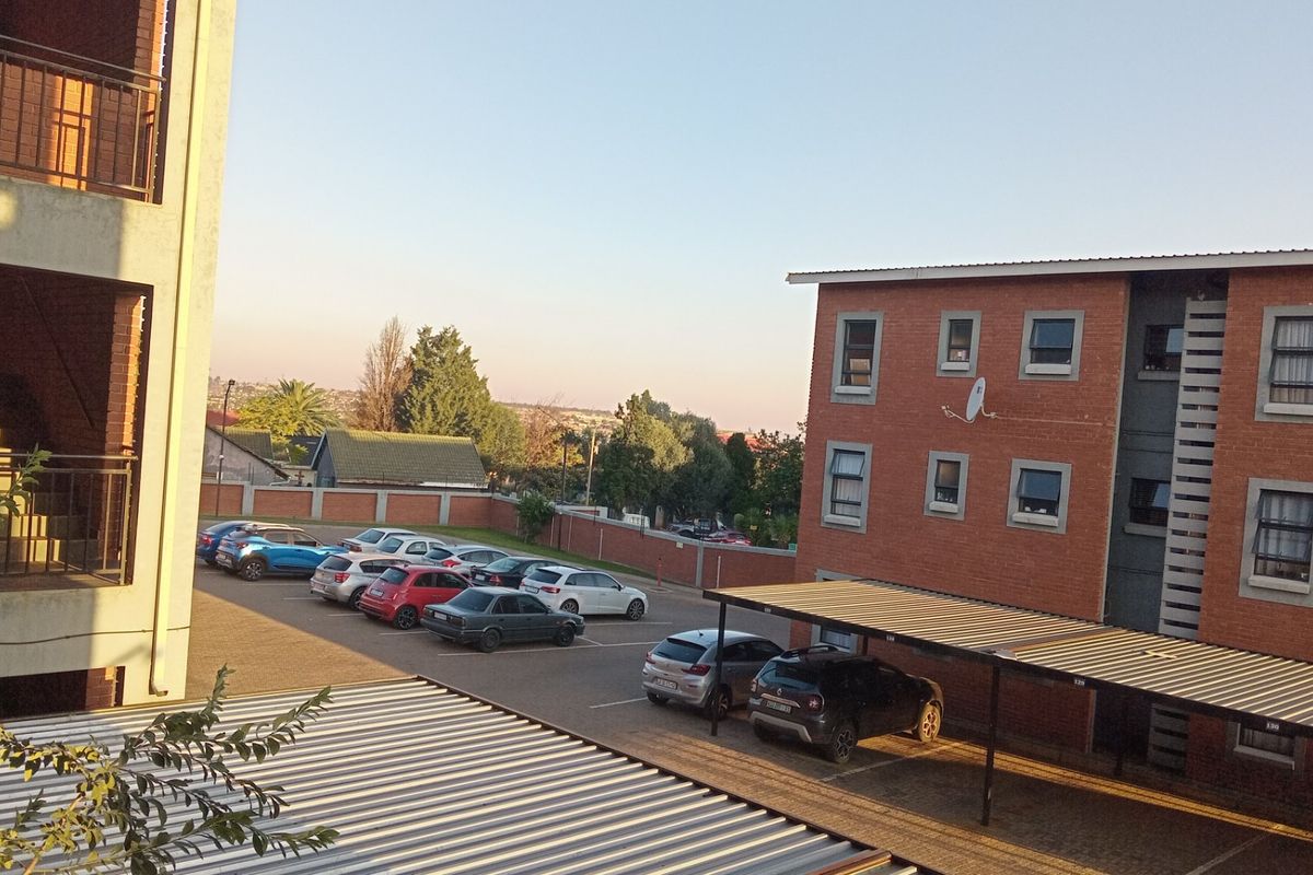 View of the apartment complex parking area featuring paved bays, covered carports, and brick building facades.