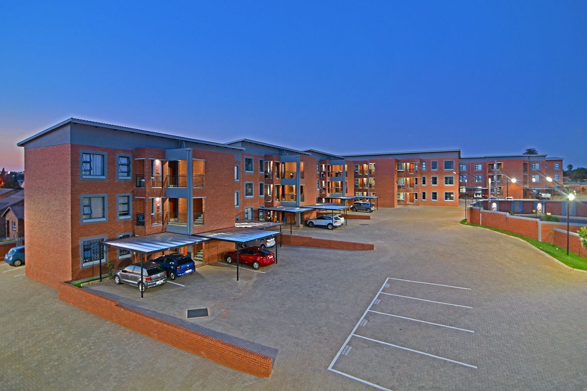 Aerial view of a modern brick apartment complex at dusk, featuring paved parking, covered carports, and multiple residential units with balconies.