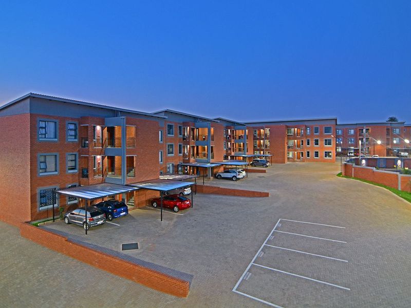Aerial view of a modern brick apartment complex at dusk, featuring paved parking, covered carports, and multiple residential units with balconies.