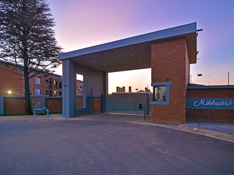 The secure entrance to Mikkadesh apartment complex featuring a modern guard house, brick facade, and automated security gate.