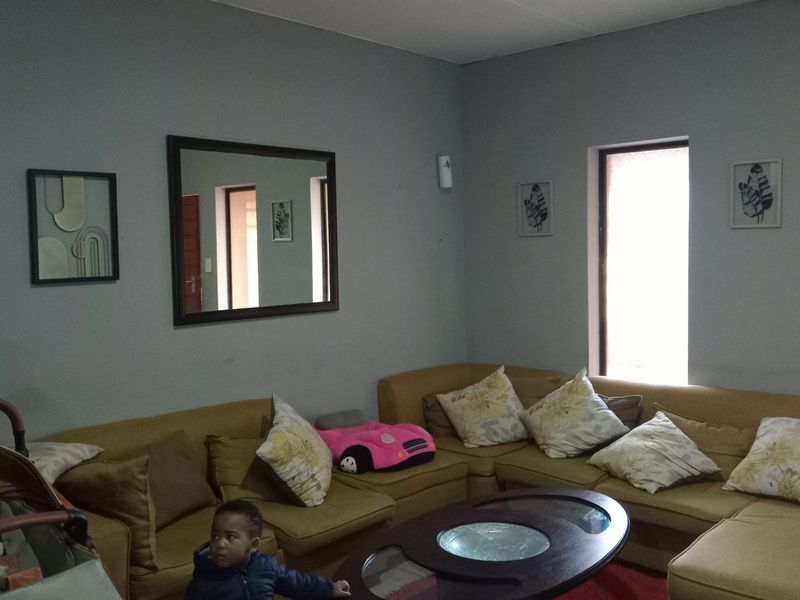 A living room area featuring neutral wall paint, natural light through windows, and access to adjacent rooms.