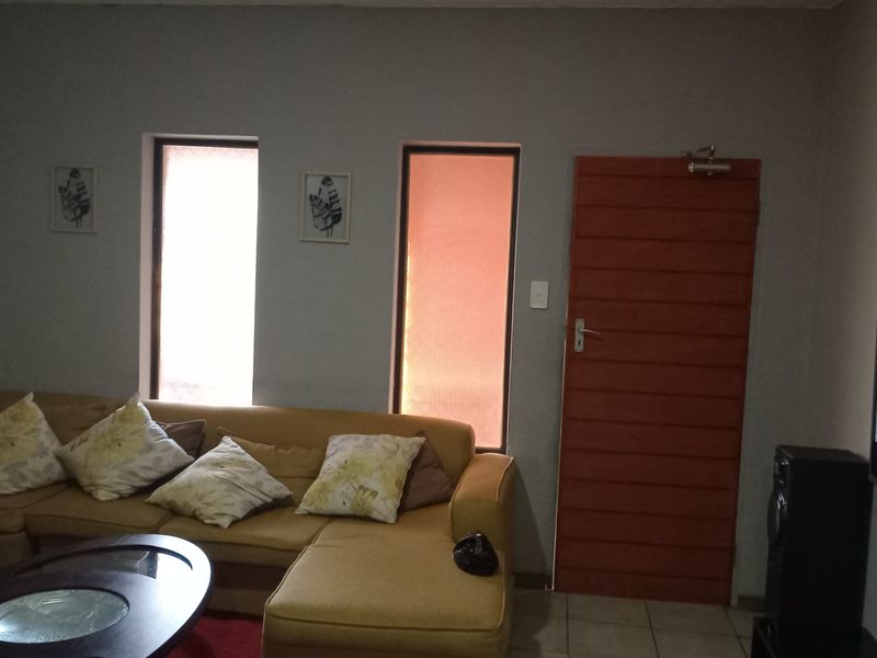A living room featuring tiled flooring, vertical windows, and a horizontal slat door, providing a functional and neutral living space.