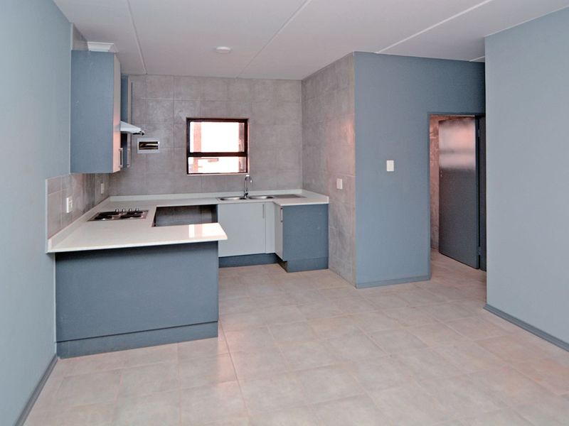 A clean, empty kitchen featuring modern blue cabinetry, stone countertops, a built-in hob, and neutral tiled flooring and splashbacks.