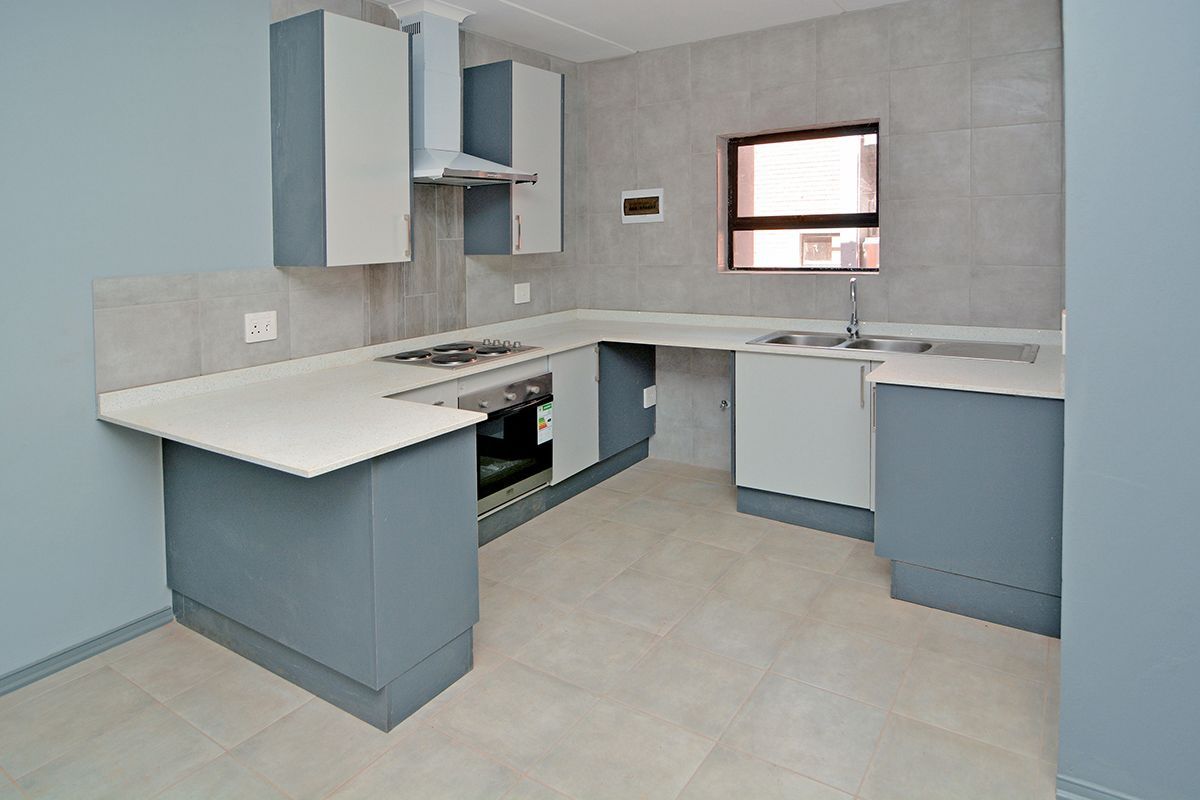 A clean, modern kitchen featuring built-in cabinetry, stone countertops, a stainless steel sink, and integrated appliances including an oven, hob, and extractor fan.