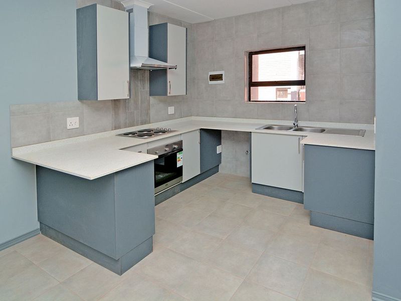 A clean, modern kitchen featuring built-in cabinetry, stone countertops, a stainless steel sink, and integrated appliances including an oven, hob, and extractor fan.