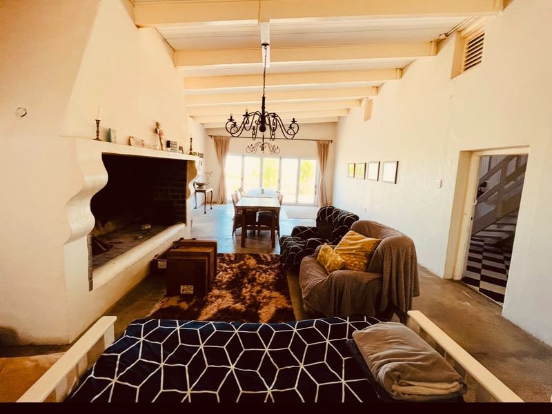 Spacious open-plan living and dining area featuring a large masonry fireplace, exposed timber beam ceilings, and direct access to the outdoors via sliding doors.