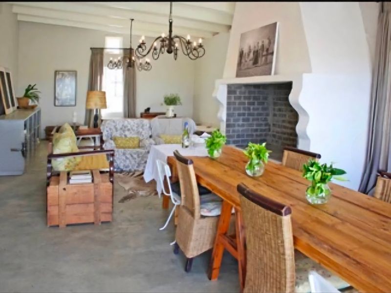 Spacious open-plan living and dining area featuring a large masonry fireplace, exposed beam ceilings, and polished concrete flooring.