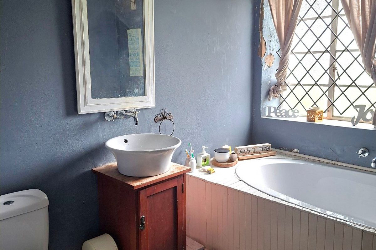 A bathroom featuring a vessel sink, built-in bathtub, and checkered flooring, requiring maintenance to the wall finishes and bathtub paneling.
