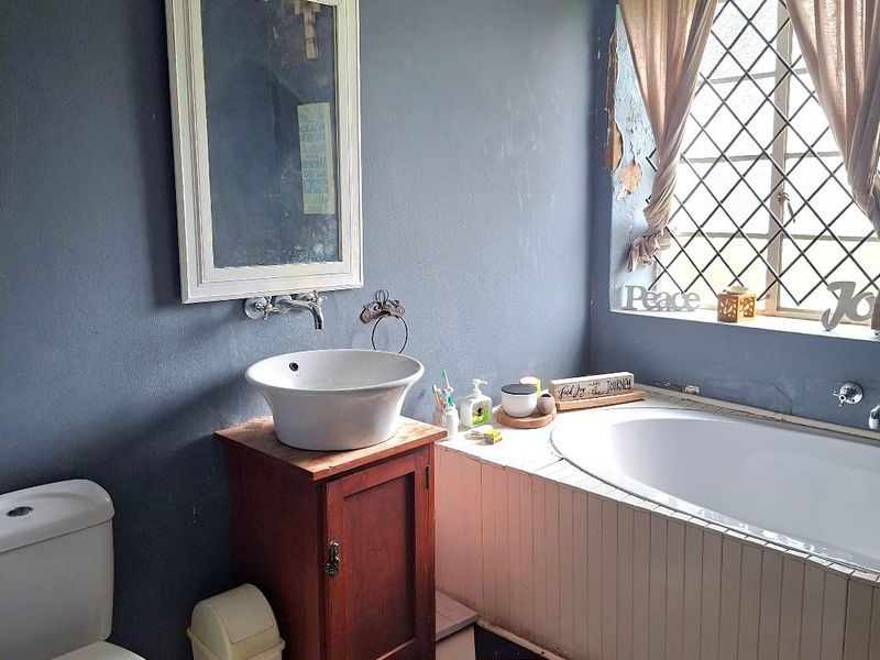 A bathroom featuring a vessel sink, built-in bathtub, and checkered flooring, requiring maintenance to the wall finishes and bathtub paneling.