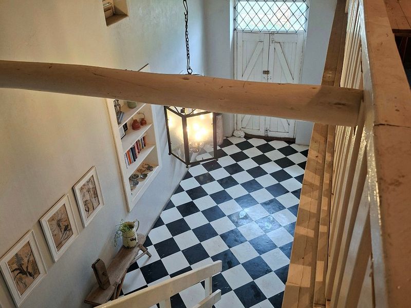 An inviting entryway featuring classic black and white checkered flooring, exposed timber ceiling beams, and a wooden staircase with a matching balustrade.