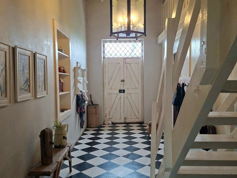 Welcoming entrance hall featuring classic checkered tile flooring, a timber staircase, and a high vaulted ceiling with a decorative hanging lantern.