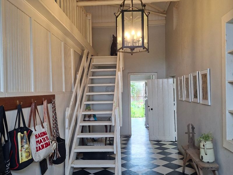 Entrance hall featuring a striking checkerboard floor, a wooden staircase leading to a mezzanine level, and exposed timber ceiling beams with a classic pendant light.