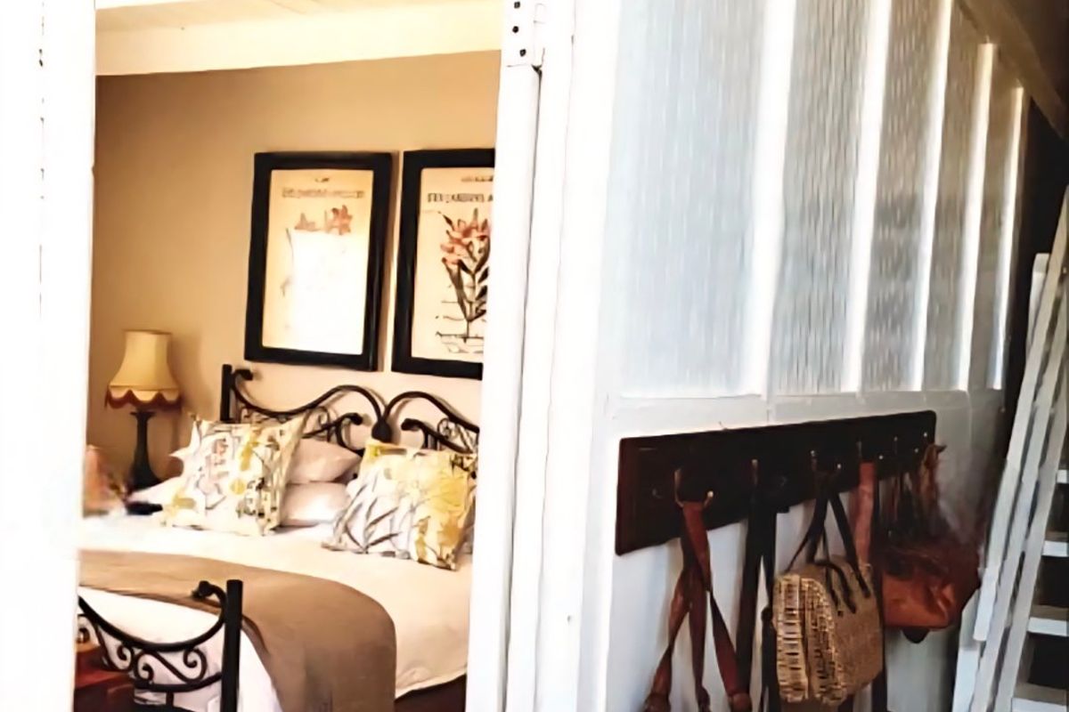 A cozy bedroom featuring exposed timber ceiling beams and classic wainscoting, viewed from an adjacent hallway with a wall-mounted coat rack.