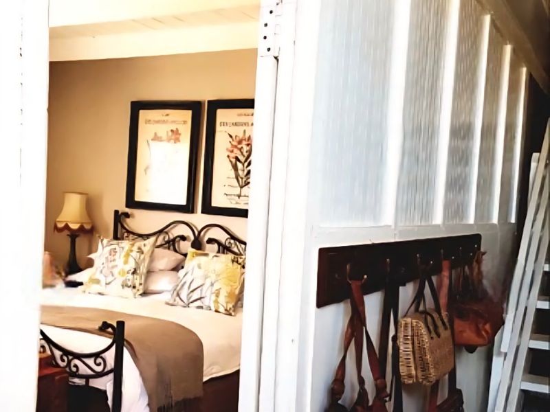 A cozy bedroom featuring exposed timber ceiling beams and classic wainscoting, viewed from an adjacent hallway with a wall-mounted coat rack.