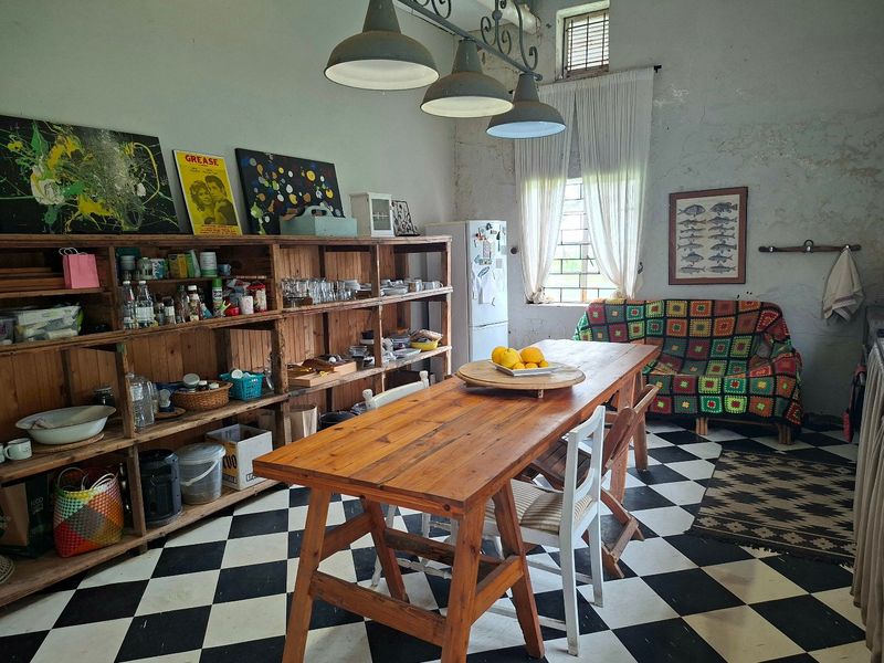 A rustic kitchen area featuring distinctive checkerboard flooring, industrial pendant lighting, and built-in wooden shelving, showing signs of wear on the wall finishes.