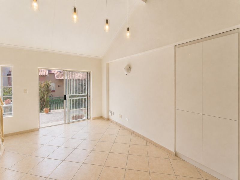 A bright, empty living room featuring vaulted ceilings, tiled floors, built-in storage cupboards, and a sliding glass door leading to an outdoor area.