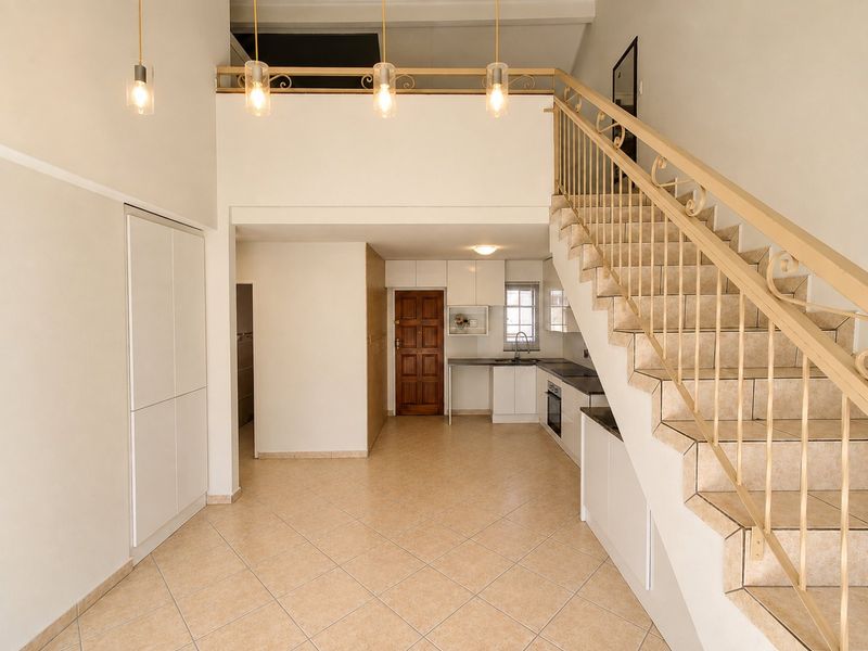 Open-plan living area featuring a tiled floor, staircase with metal balustrade, mezzanine level, and a functional kitchen with built-in cabinetry and appliances.