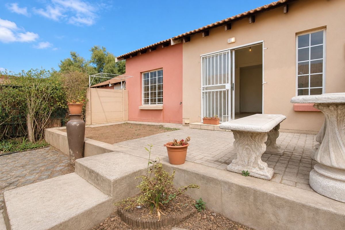 Rear exterior view of the townhouse featuring a paved patio area, concrete steps, and a security gate leading into the home.