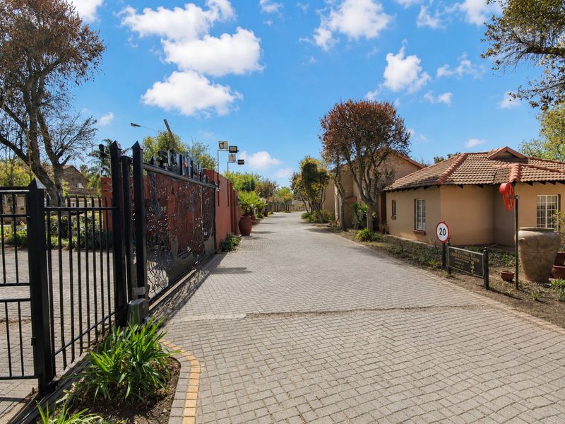 A view of the secure entrance and paved driveway leading into the townhouse complex, featuring well-maintained perimeter walls and established landscaping.