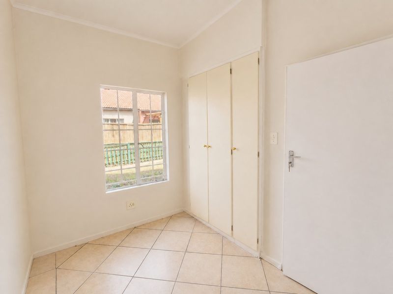 A clean, empty bedroom featuring neutral tiled flooring, built-in cupboards, and a window providing natural light.