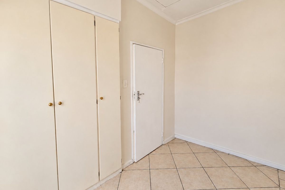 A clean, empty bedroom featuring neutral tiled flooring, built-in cupboards, and a ceiling access hatch, providing a blank canvas for personalization.