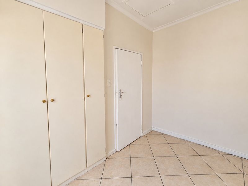 A clean, empty bedroom featuring neutral tiled flooring, built-in cupboards, and a ceiling access hatch, providing a blank canvas for personalization.