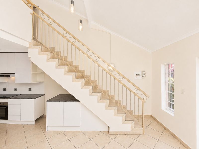 An open-plan living area featuring a modern staircase with metal balustrade, under-stair storage, and a compact, well-maintained kitchen with built-in appliances.