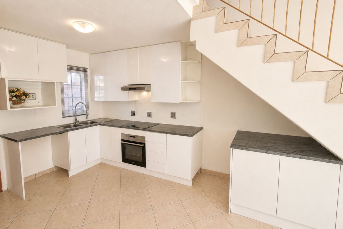 Modern kitchen featuring white cabinetry, dark laminate countertops, built-in oven and hob, and tiled flooring, situated beneath an open staircase.