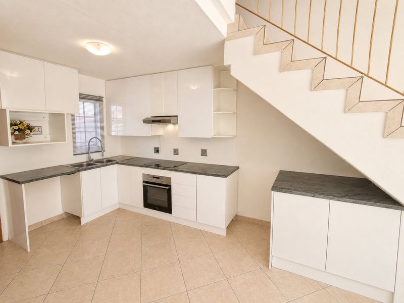 Modern kitchen featuring white cabinetry, dark laminate countertops, built-in oven and hob, and tiled flooring, situated beneath an open staircase.