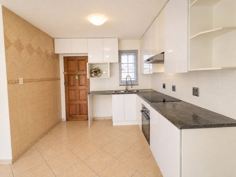 A clean, functional kitchen featuring white cabinetry, dark laminate countertops, built-in oven and hob, and neutral tiled flooring.