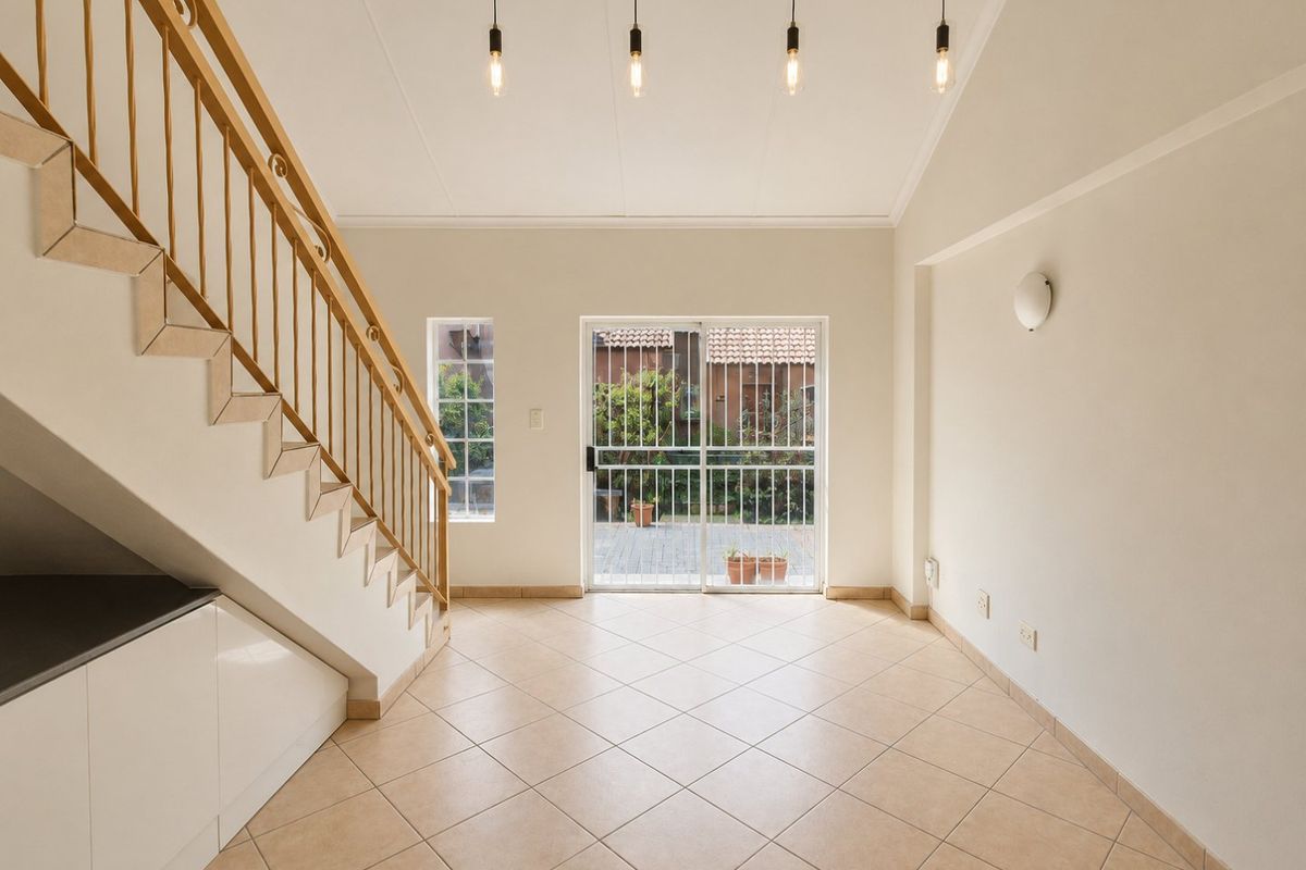 Bright and spacious living area featuring tiled floors, modern pendant lighting, and a staircase with built-in under-stair storage, leading to a rear patio.