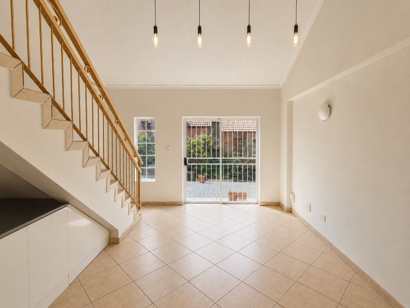 Bright and spacious living area featuring tiled floors, modern pendant lighting, and a staircase with built-in under-stair storage, leading to a rear patio.