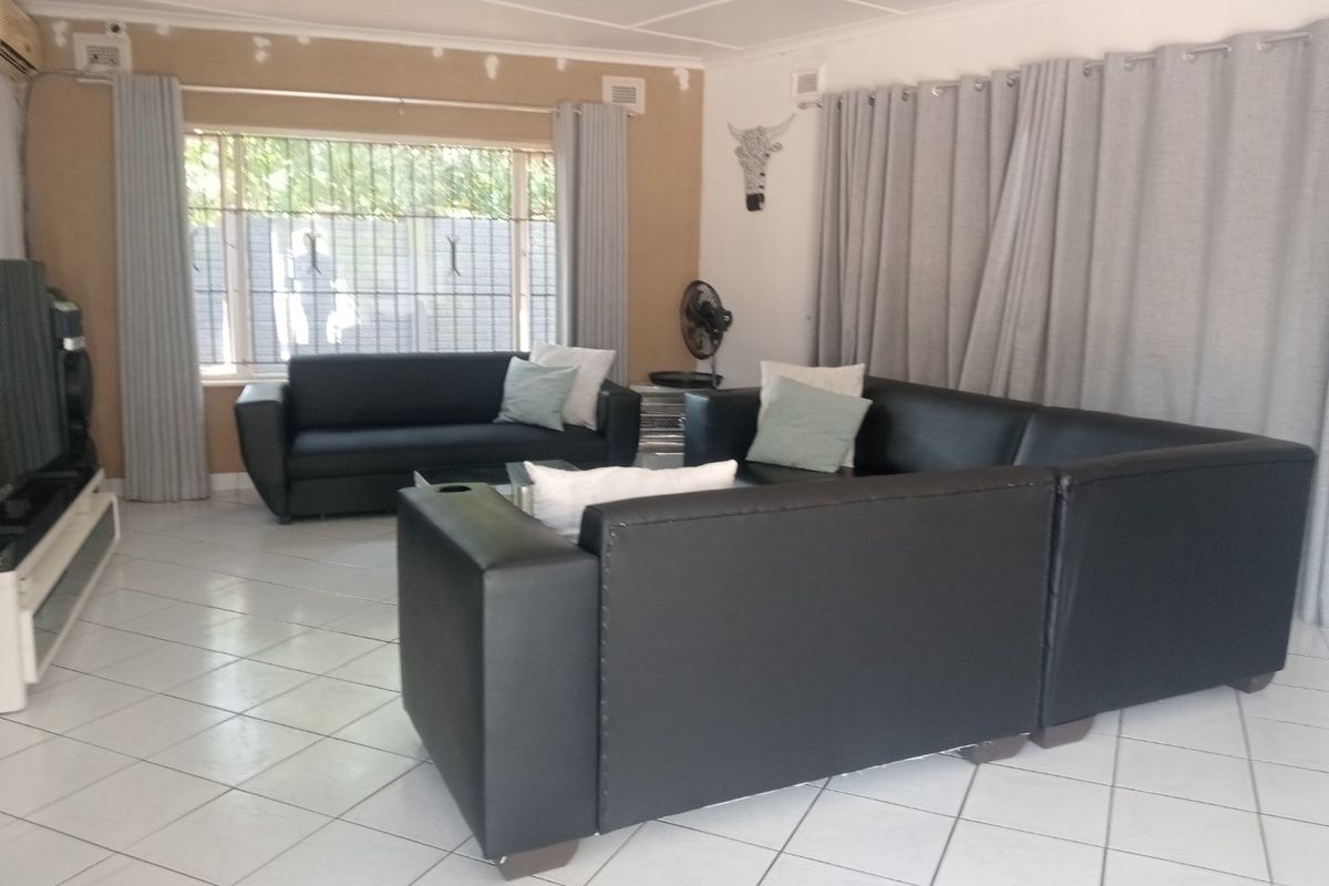 A living room featuring tiled flooring, security bars on windows, and an air conditioning unit, with some visible wall maintenance required.