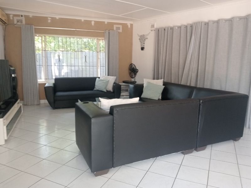 A living room featuring tiled flooring, security bars on windows, and an air conditioning unit, with some visible wall maintenance required.