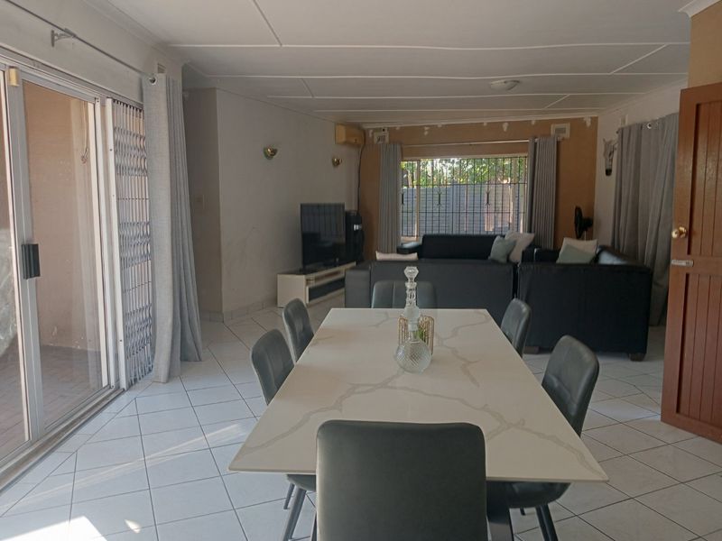 Open-plan living and dining area featuring tiled flooring, sliding door access to the patio, and wall-mounted air conditioning.