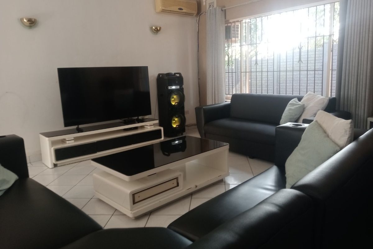 A living room featuring tiled flooring, wall sconces, and a wall-mounted air conditioning unit, with security bars installed on the window.