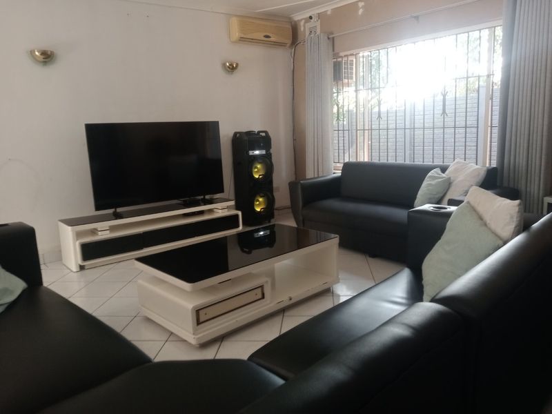 A living room featuring tiled flooring, wall sconces, and a wall-mounted air conditioning unit, with security bars installed on the window.