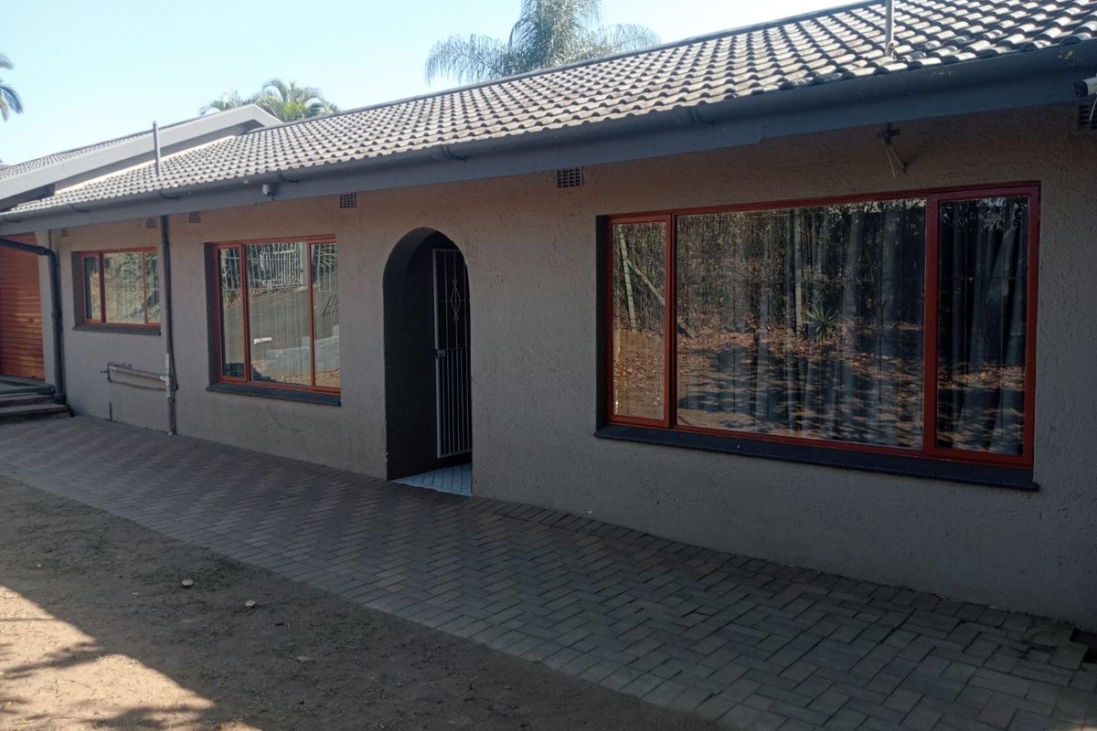 Rear exterior view of the house featuring a paved walkway, tiled roof, and large windows with dark frames.