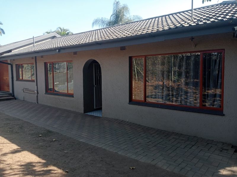 Rear exterior view of the house featuring a paved walkway, tiled roof, and large windows with dark frames.