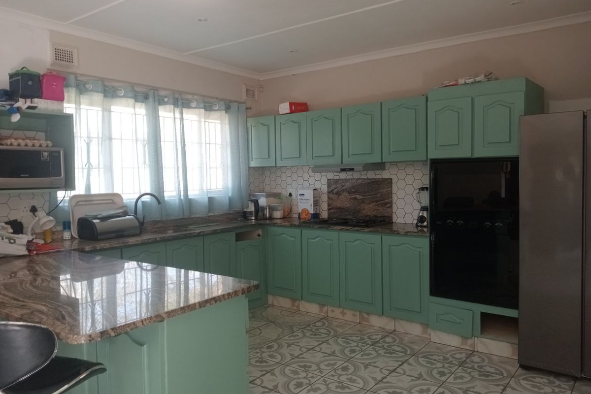 A functional kitchen featuring green cabinetry, granite countertops, a hexagonal tile backsplash, and patterned floor tiles with ample storage space.