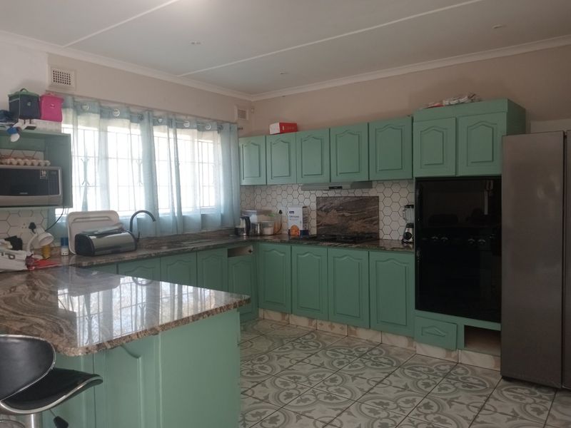 A functional kitchen featuring green cabinetry, granite countertops, a hexagonal tile backsplash, and patterned floor tiles with ample storage space.